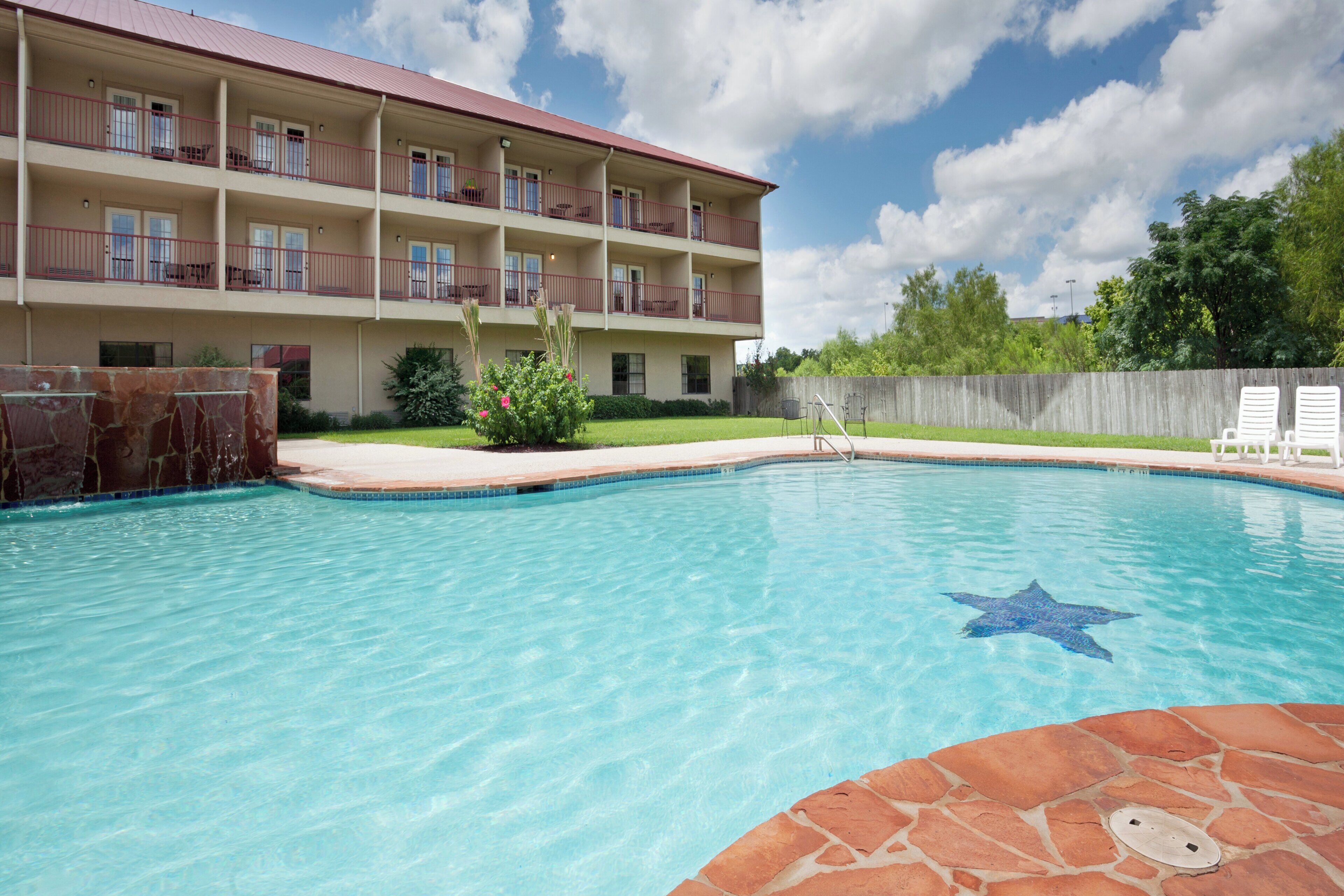 Un hotel con piscina, terraza de piedra y valla de madera.
