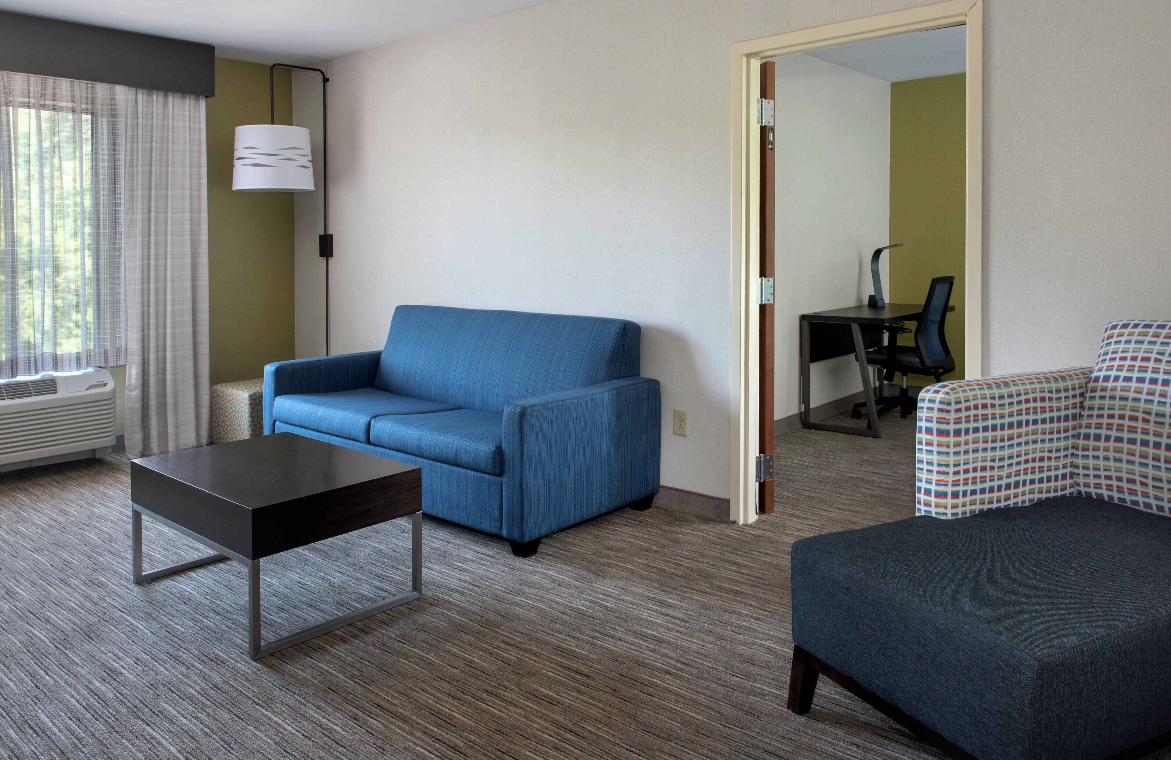 A hotel room with a blue sofa, a small table, a patterned armchair, and a desk with a chair.
