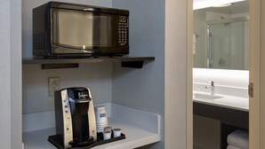 Uma cozinha compacta com micro-ondas, cafeteira e xícaras de café.