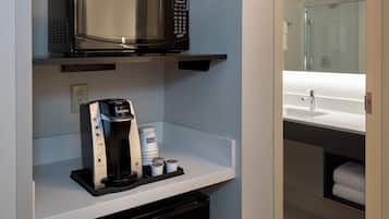 Une petite cuisine équipée d’un four à micro-ondes, d’une machine à café et de tasses à café, le tout posé sur un plan de travail blanc.