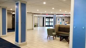 Un hall de hotel con mostrador de recepción, un área de espera con sofá y sillones, y una señal de salida.
