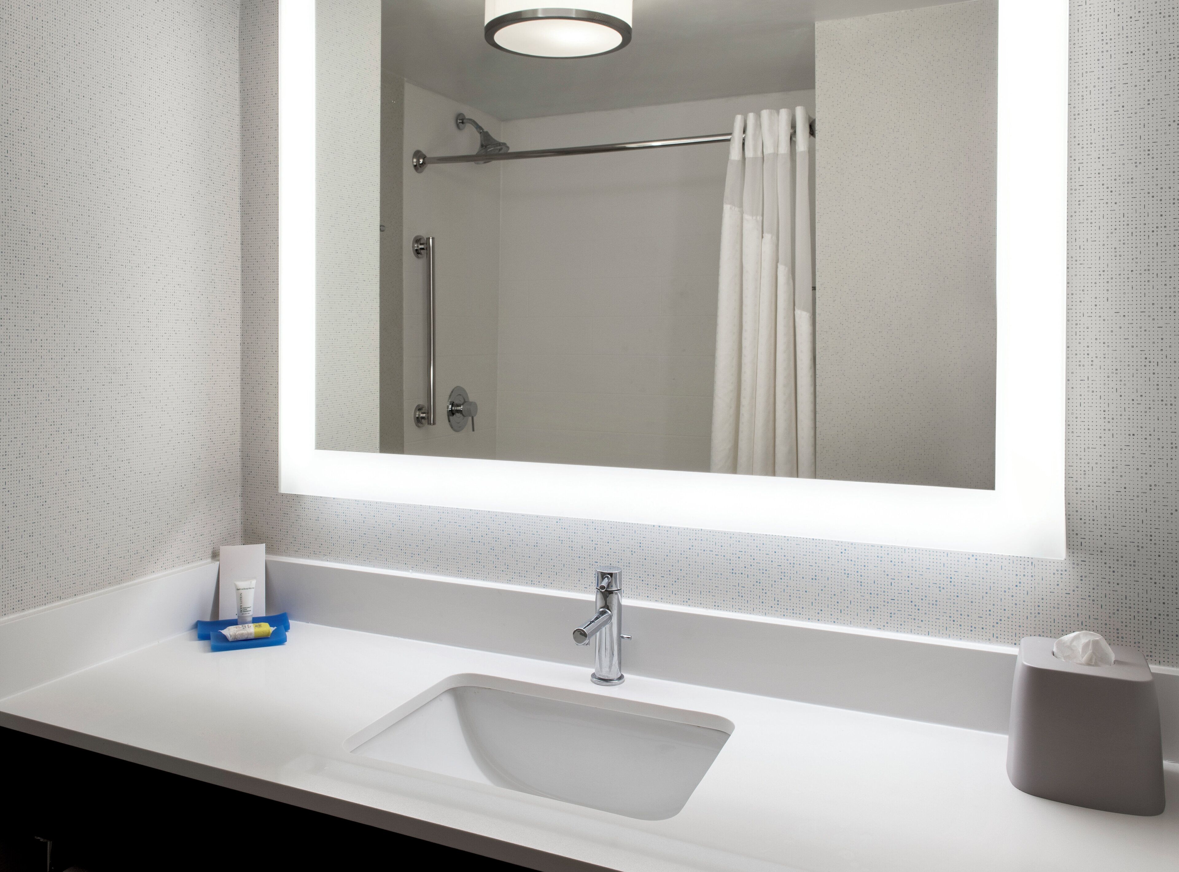 Une salle de bain avec un lavabo blanc, un miroir, un porte-serviettes et un rideau de douche.