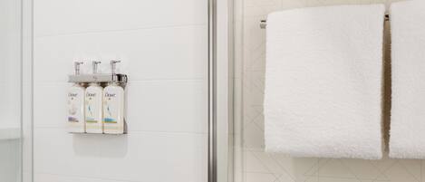 Un baño con azulejos blancos, una puerta de cristal para la ducha y tres botellas de Dove.