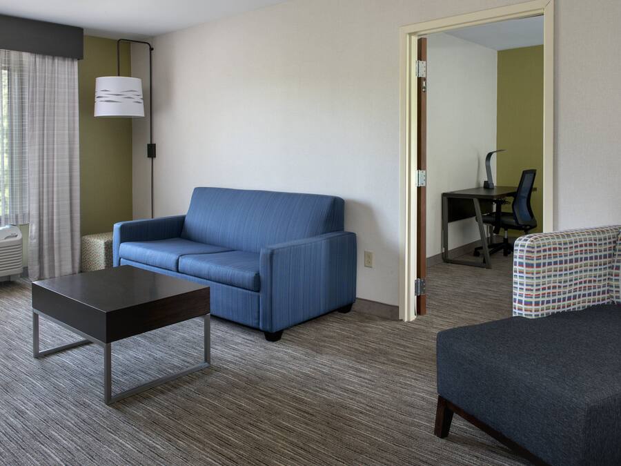 A hotel room with a blue sofa, a small table, a patterned armchair, and a desk with a chair.