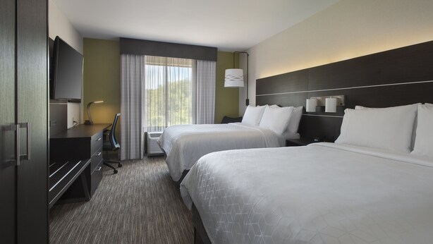 Quarto de hotel com duas camas, uma escrivaninha, televisão e janela com cortinas.