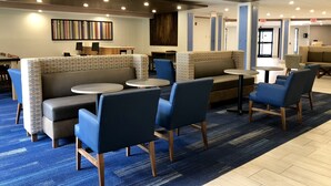 Um saguão moderno de hotel com áreas de estar, mesas e uma recepção.