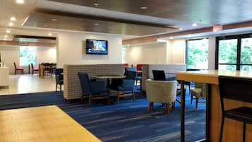 A hotel lobby with seating areas, a television mounted on the wall, and large windows providing natural light.