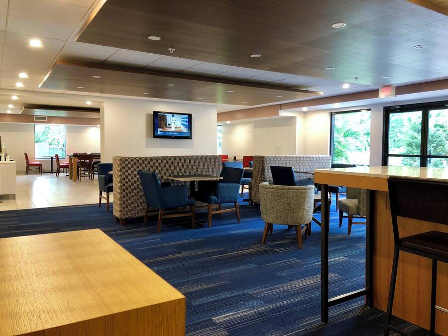 A hotel lobby with seating areas, a television mounted on the wall, and large windows providing natural light.