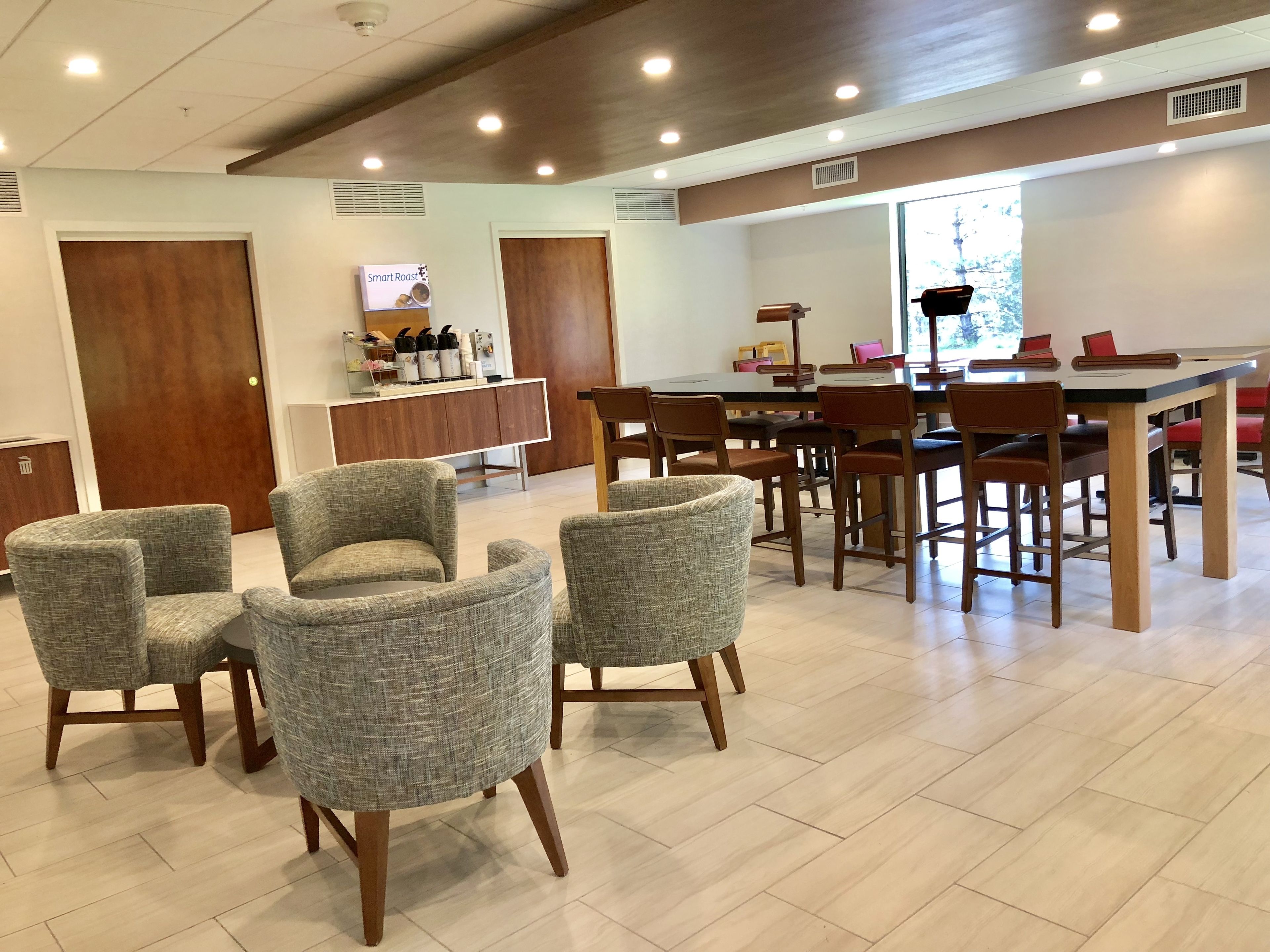 Un espace repas moderne avec une table et des chaises en bois, un comptoir équipé d’appareils de cuisine et une vue sur l’extérieur.