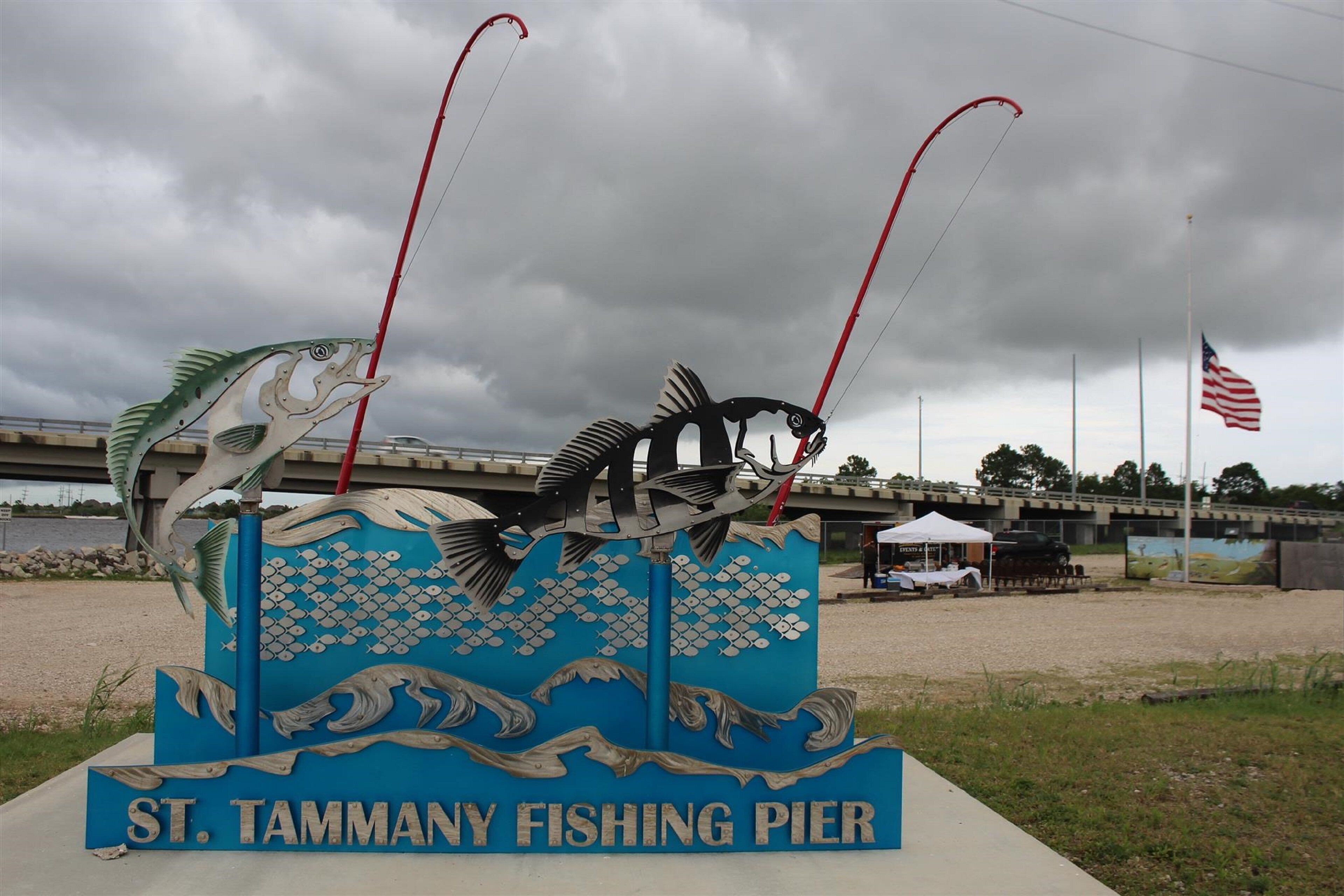 Señal de muelle de pesca con una gran escultura de pez y cañas de pescar.