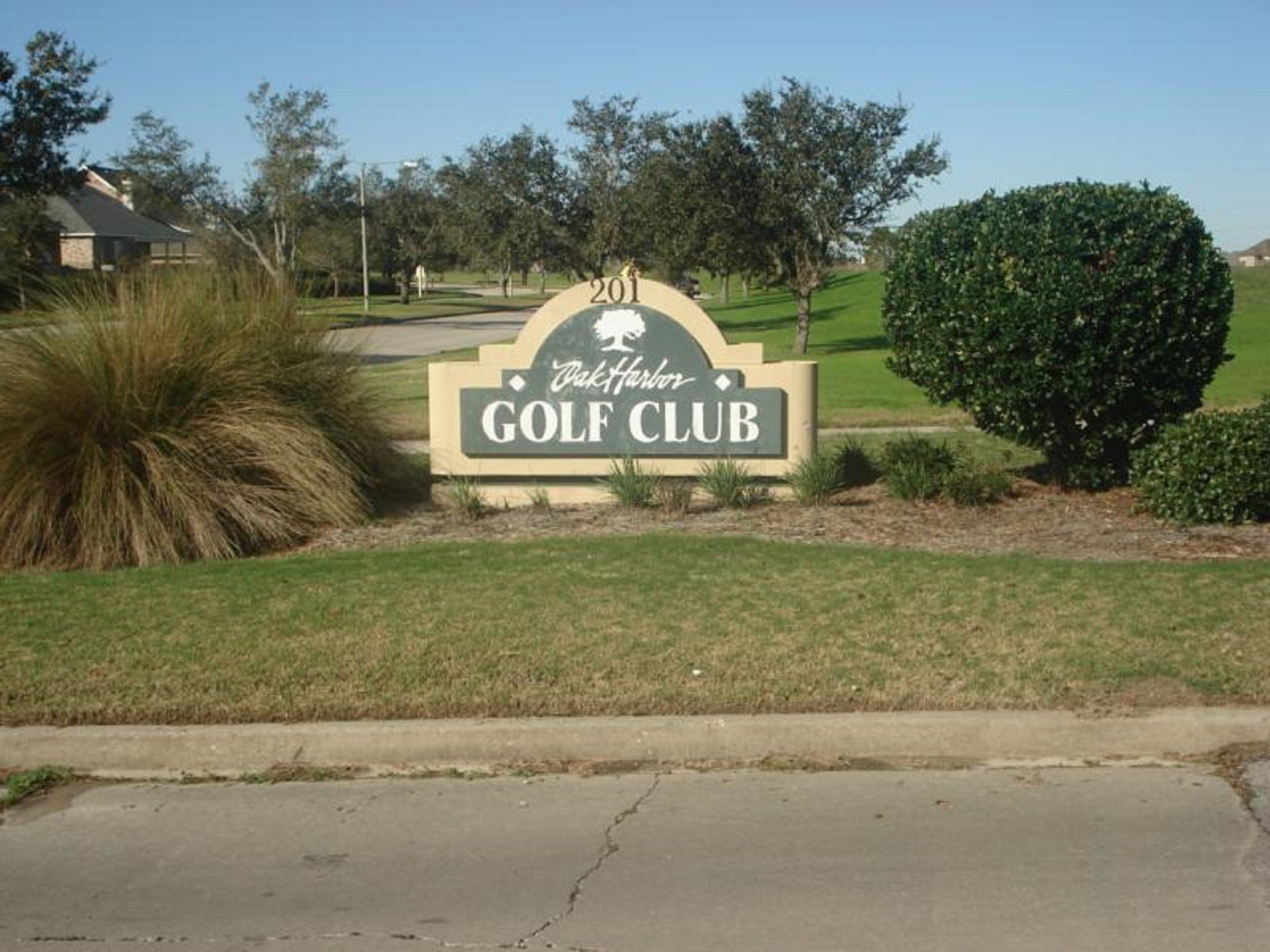 En skylt för en golfklubb med en logotyp, omgiven av välskött gräs och några träd.