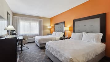 A hotel room with two beds, a desk, a chair, and a large window with curtains.