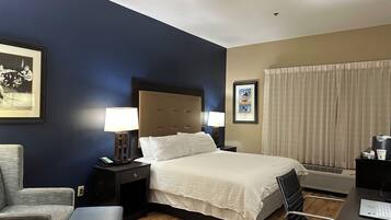 Una habitación de hotel con cama, mesitas de noche, escritorio, silla y ventana con cortinas.