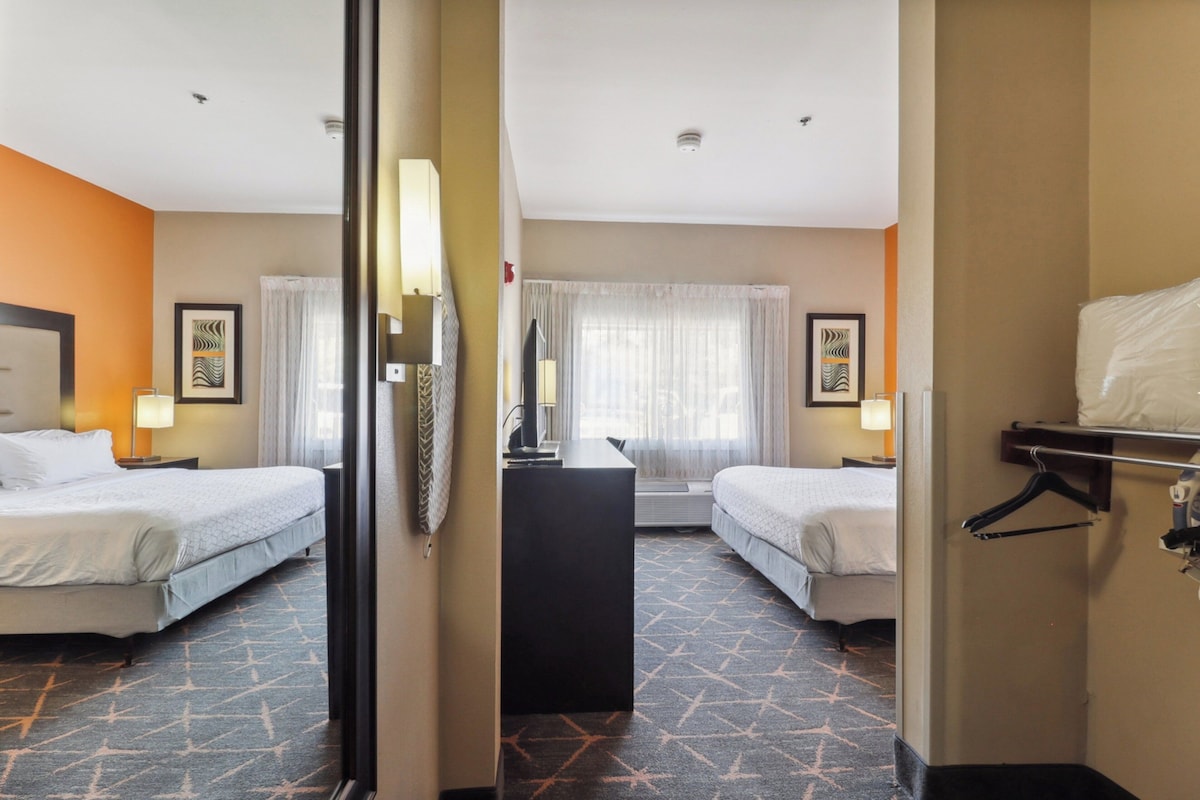 A hotel room with two beds, a desk, and a mirror.