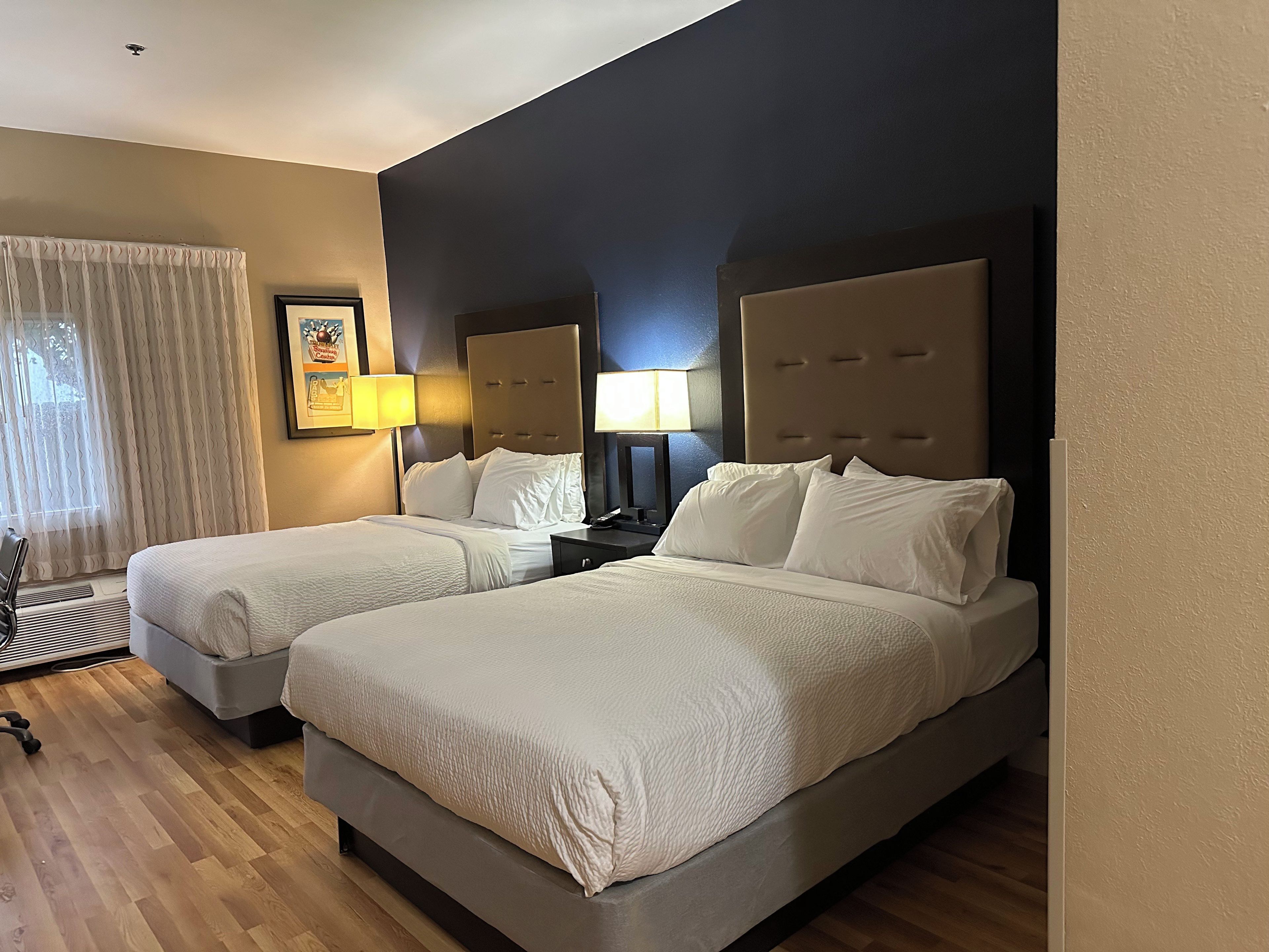 A hotel room with two beds, a desk, a chair, and a lamp.