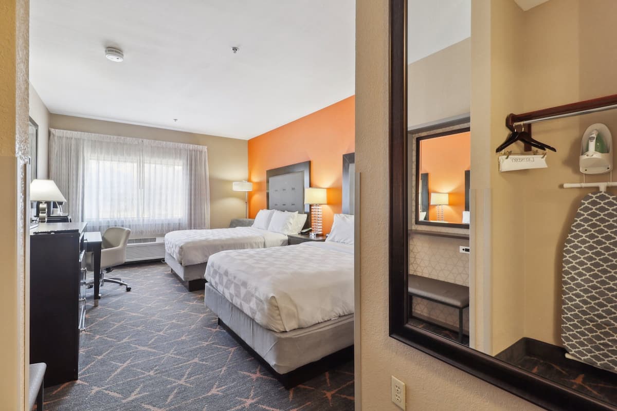 A hotel room with two beds, a desk, a chair, and a large mirror.