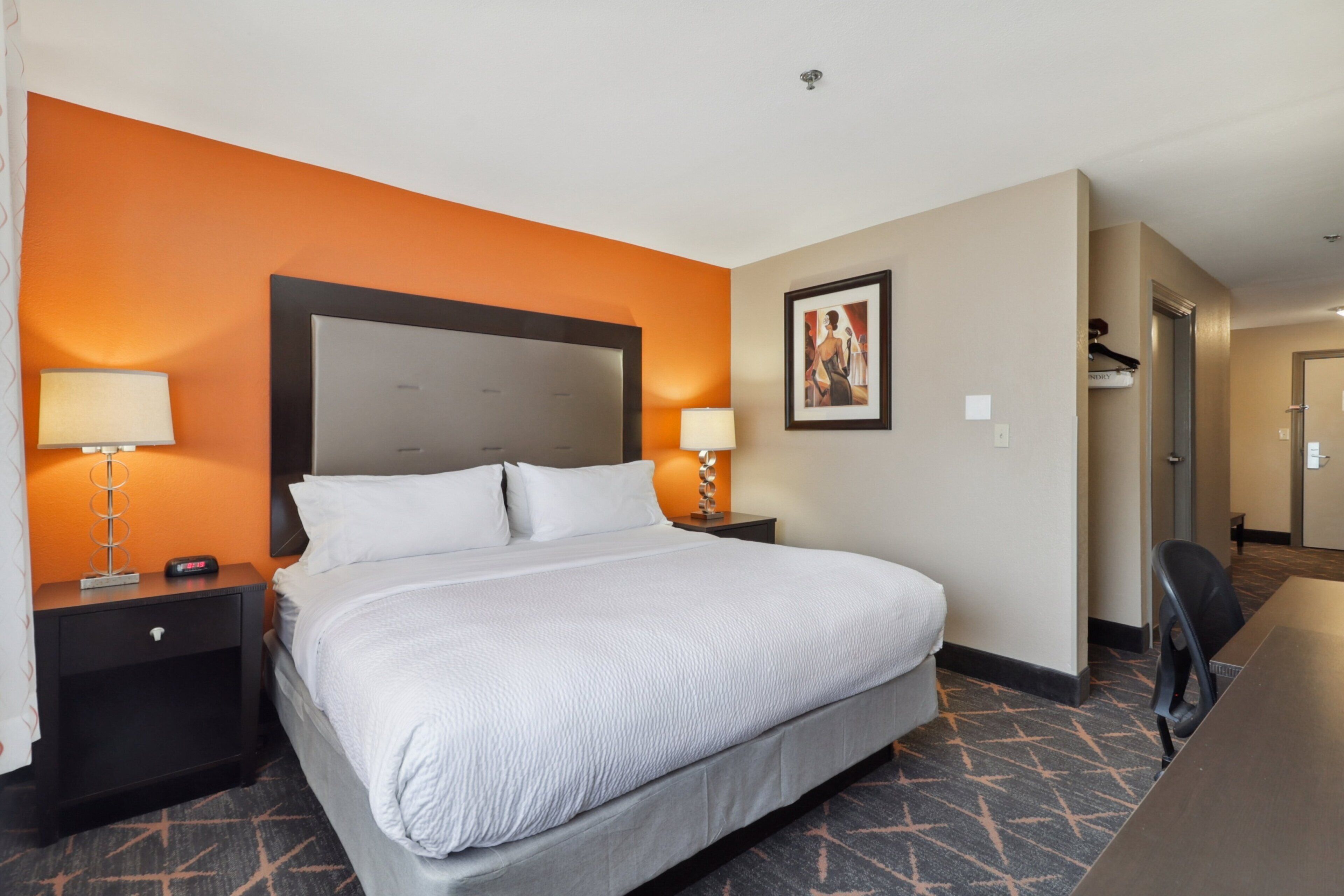 Une chambre d’hôtel avec un grand lit, deux tables de chevet avec des lampes, un tableau encadré au mur et un bureau avec une chaise.