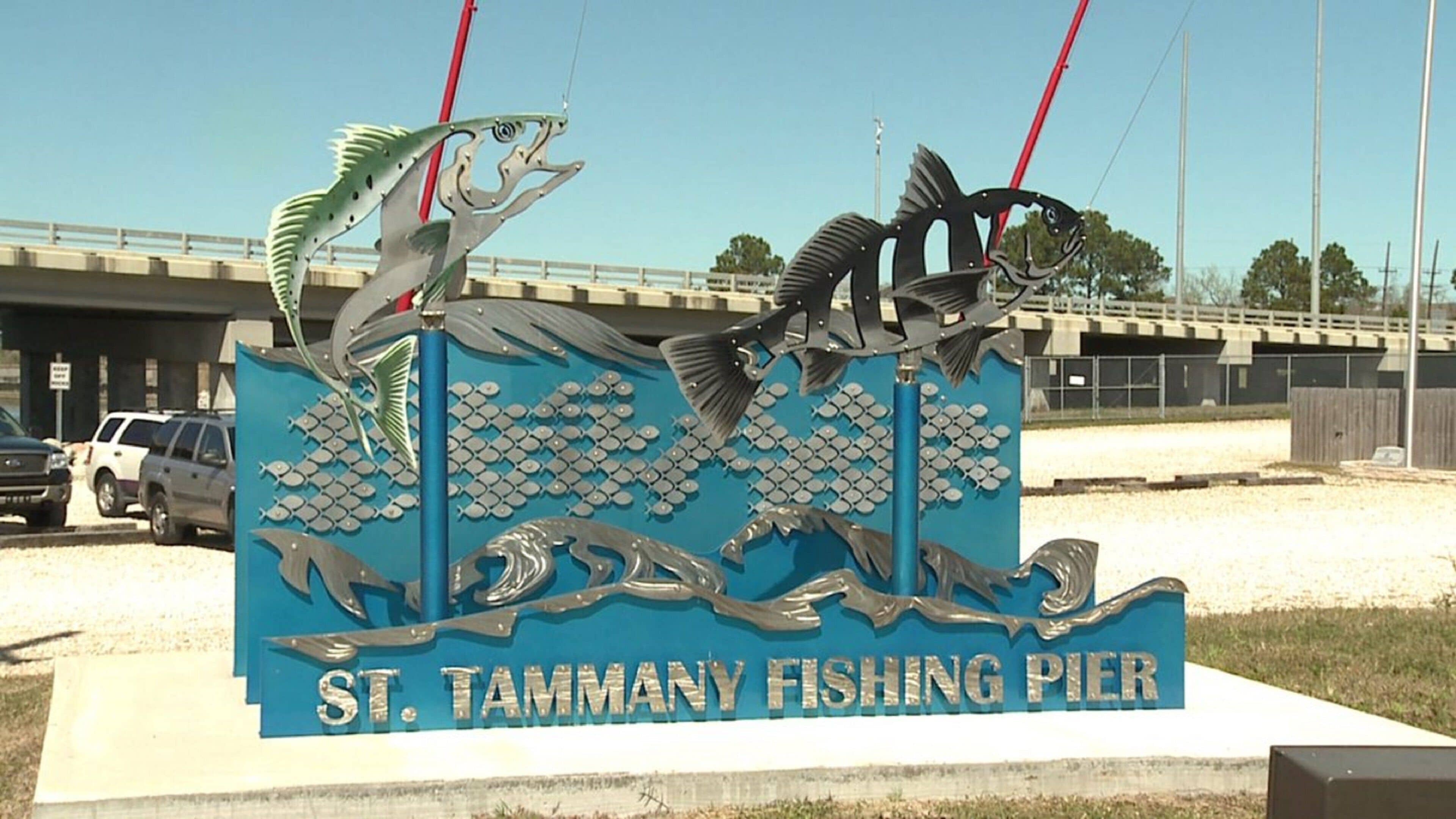 Schild für den St. Tammany Fishing Pier mit dekorativen Fischen und einer Brücke im Hintergrund.