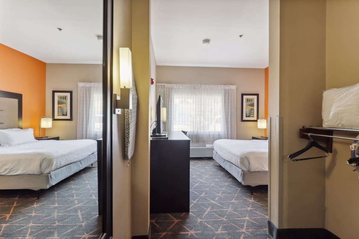 A hotel room with two beds, a desk, and a mirror.