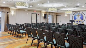 A conference room with rows of chairs, a podium with a logo, and a large window with curtains.