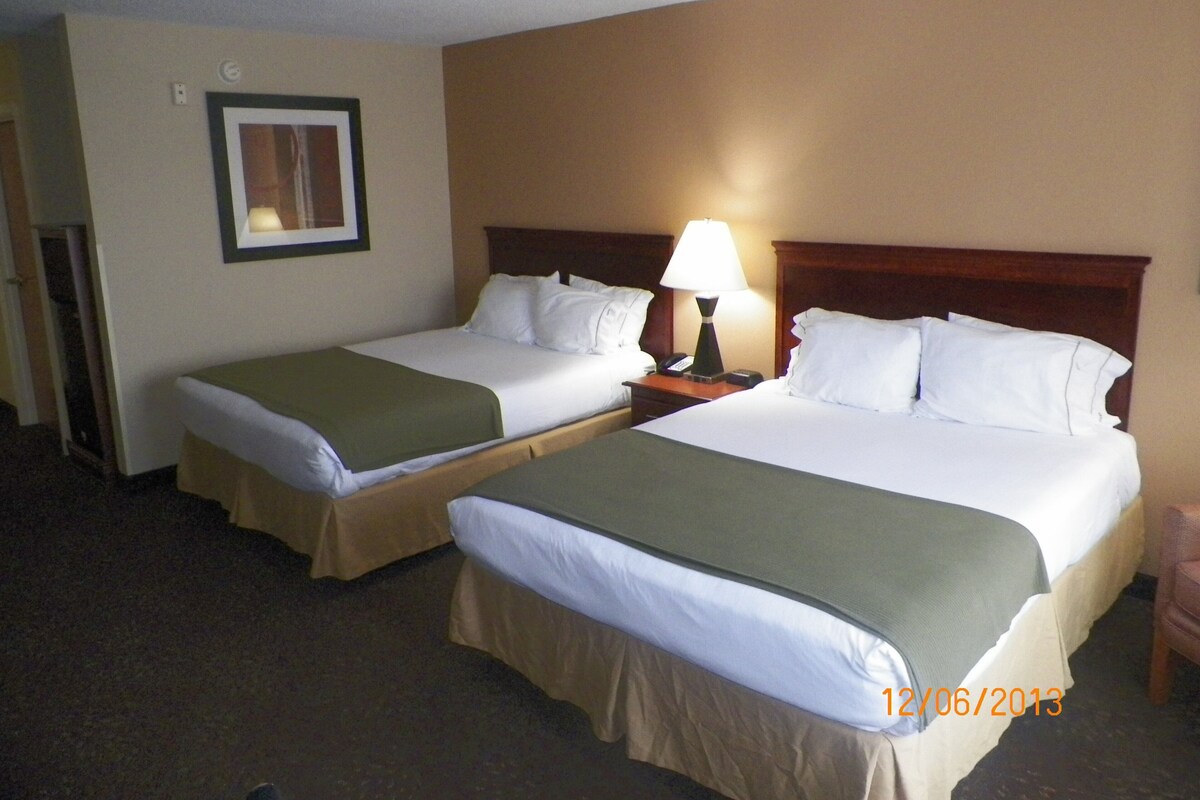 A hotel room with two beds, a nightstand with a lamp, a framed picture on the wall, and a date stamp.