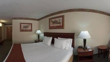 A hotel room with a large bed, two bedside tables with lamps, a small round table, and two framed pictures on the walls.