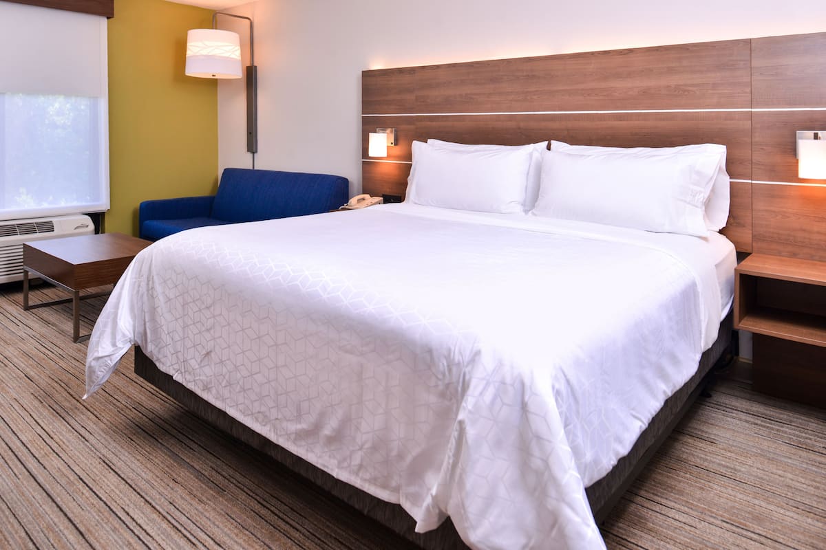 Une chambre d’hôtel avec un grand lit, un fauteuil bleu, une table de chevet avec une lampe et un téléphone fixé au mur.