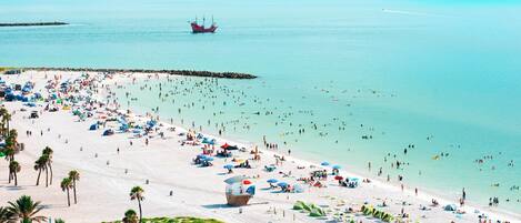 Een strand met tal van parasols en tenten, een uitkijktoren van de badmeester en een helder uitzicht op de zee.