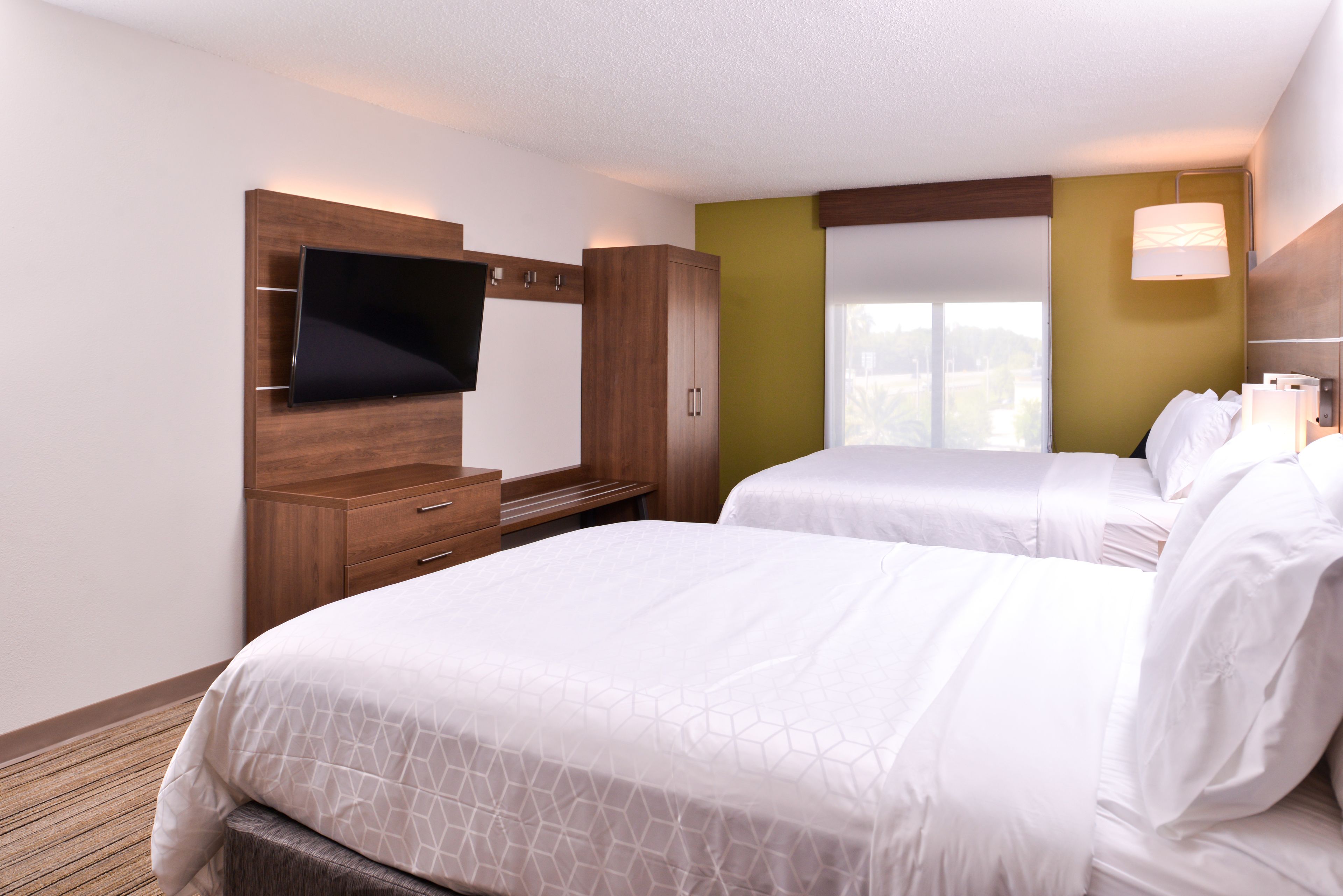 Quarto de hotel com duas camas, uma TV presa em um armário de madeira e uma janela com vista.