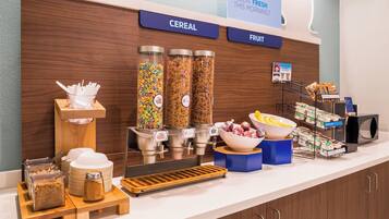 A breakfast buffet with cereal and fruit options, a coffee machine, and various breakfast items.