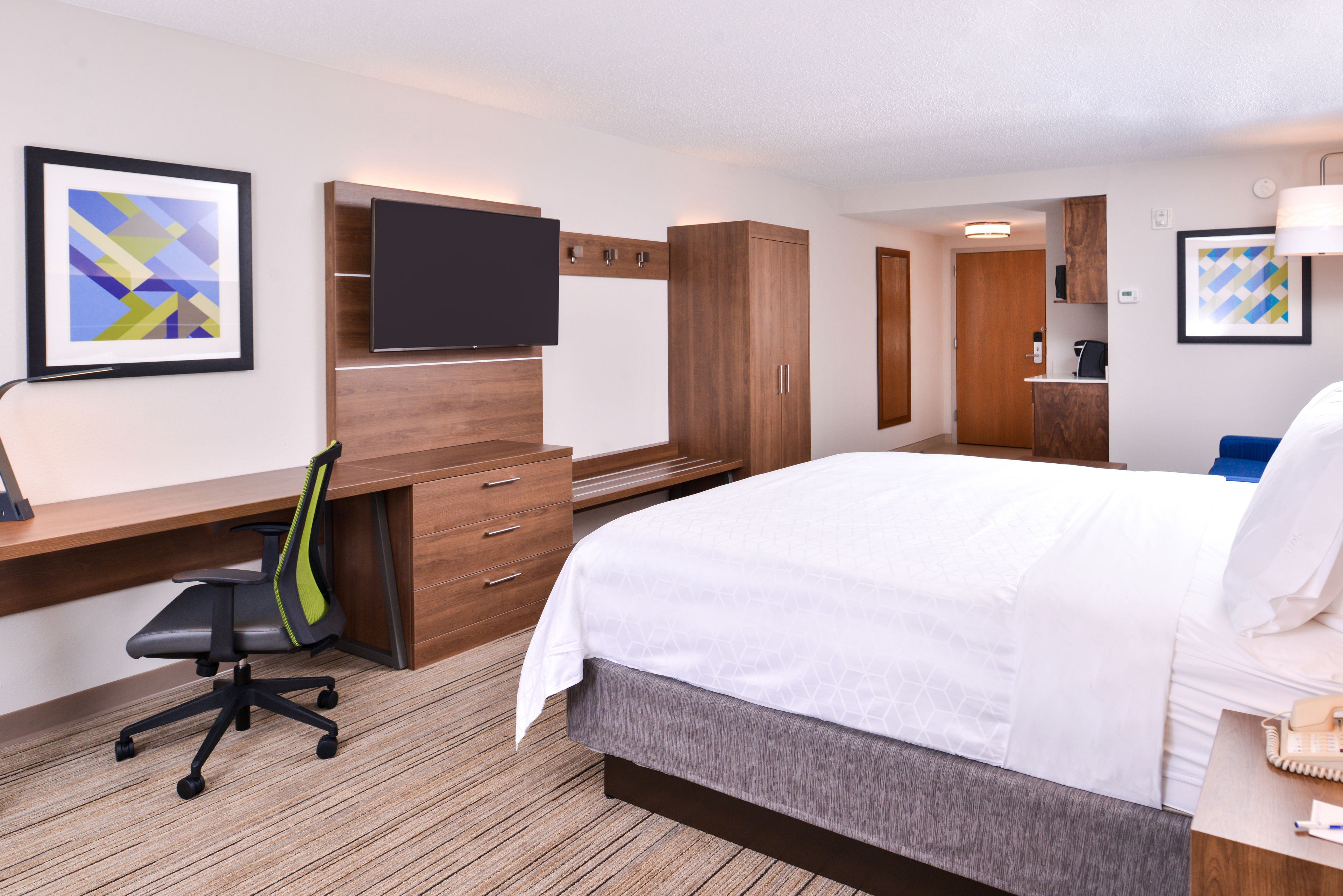 A hotel room with a bed, desk, chair, TV, wardrobe, and a bathroom.