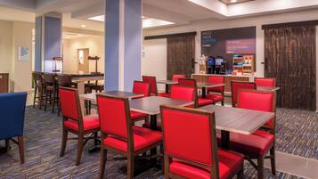 A hotel dining area with red upholstered chairs and wooden tables, a coffee station, and a sign indicating a rewards program.
