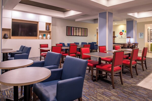 A hotel lobby with multiple seating areas, including round tables and chairs, and a large wall-mounted TV. - Holiday Inn Express Hotel & Suites Tampa-Anderson Rd/Veteran by IHG (Tampa)