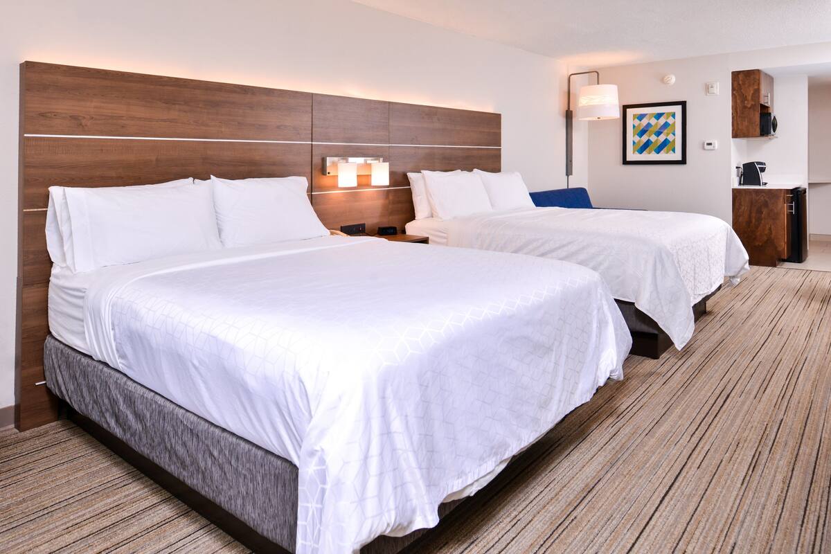 Une chambre d’hôtel avec deux lits, une tête de lit en bois, des lampes de chevet, un tableau encadré et un petit bureau avec une chaise.