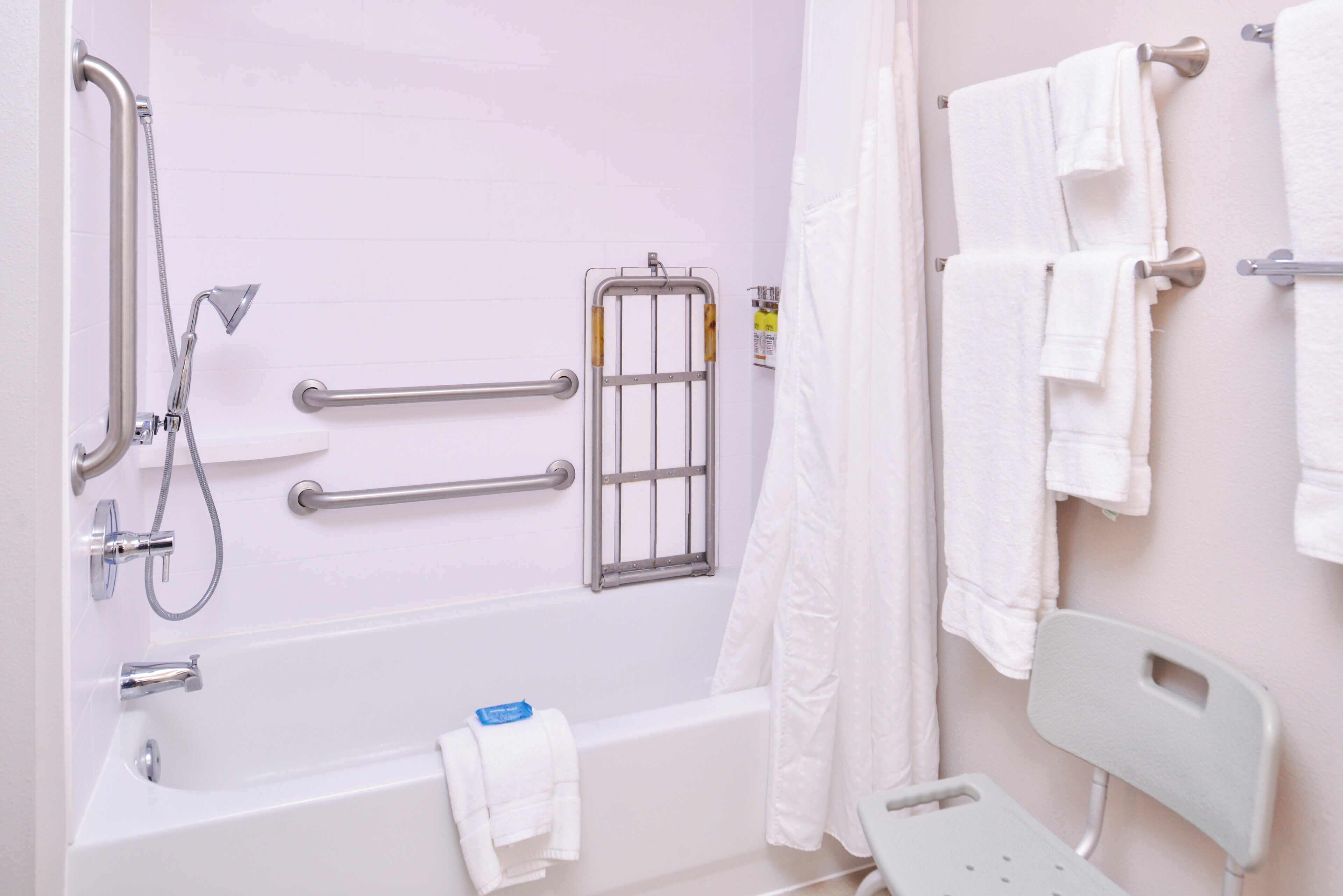 A bathroom with a bathtub, grab bars, a shower, and multiple towels.