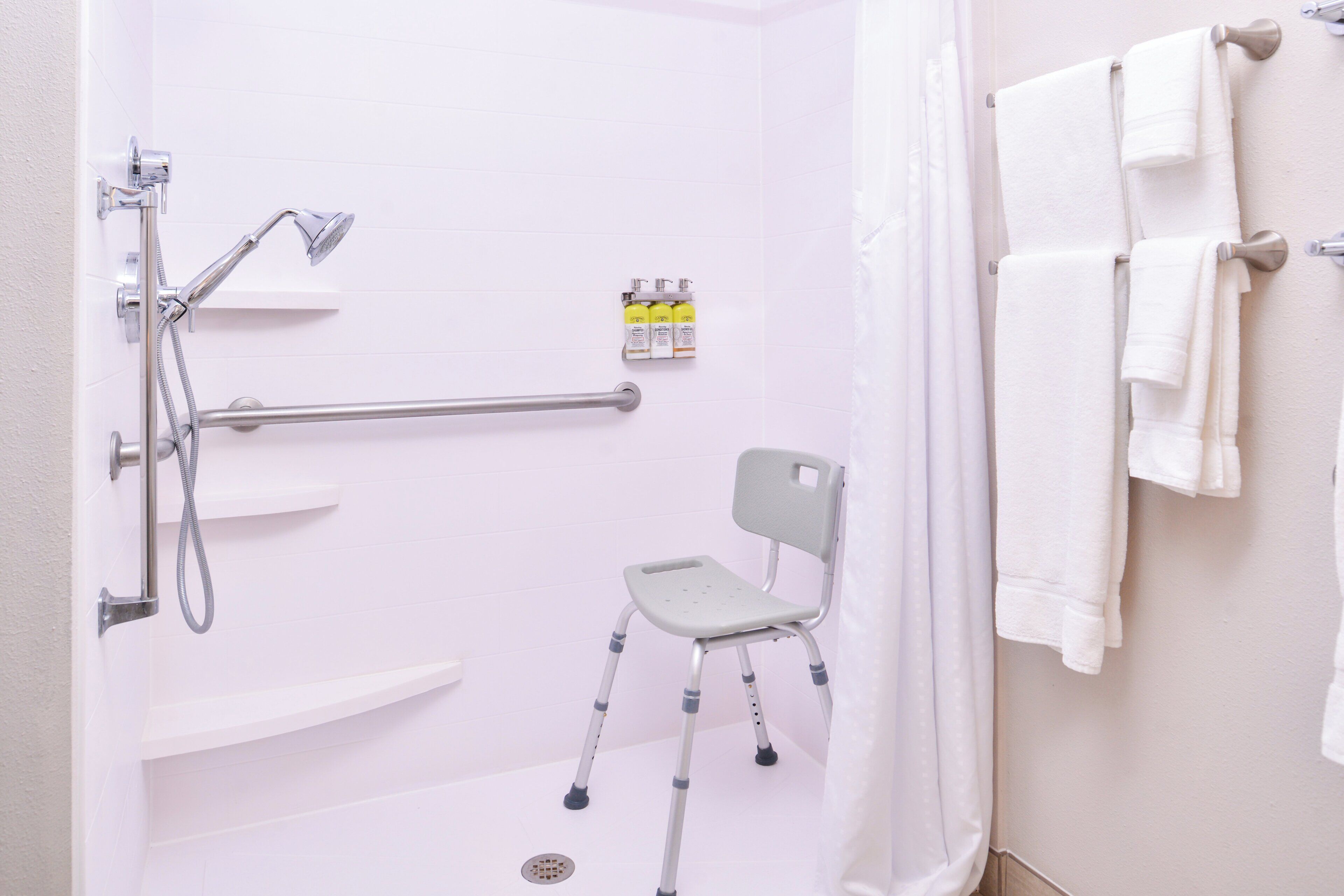 A bathroom with a shower, grab bars, a wheelchair, and a towel rack.