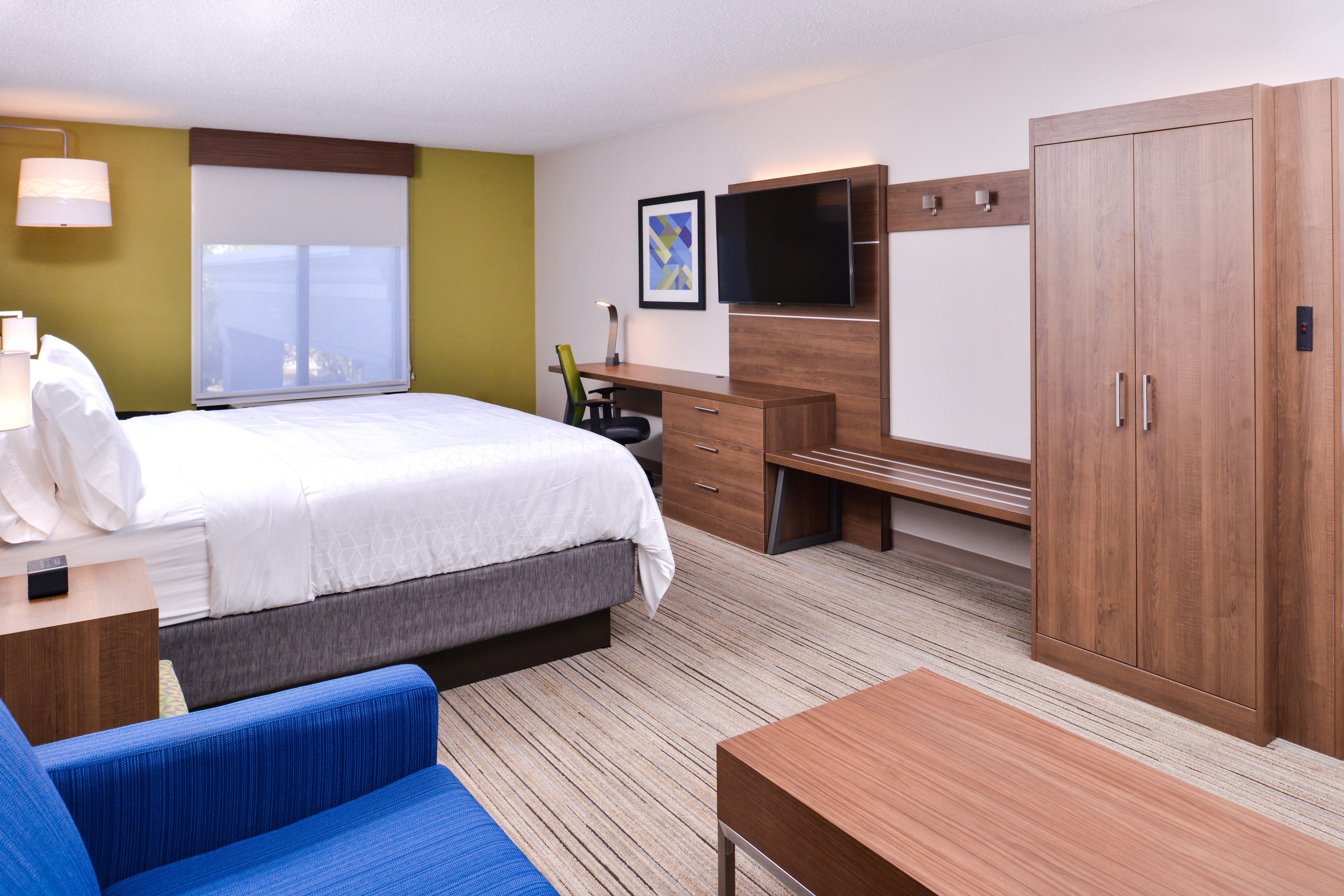 Hotellihuone, jossa on sänky, työpöytä, tuoli, televisio ja vaatekaappi.