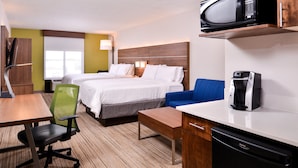 A hotel room with two beds, a desk, a chair, a microwave, a coffee maker, and a dishwasher.
