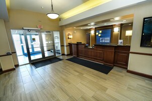 Un vestíbulo de hotel con mostrador de recepción, puerta de cristal y suelo de madera.