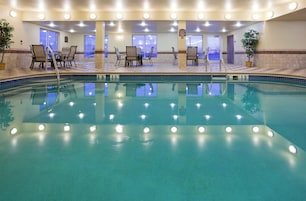 Una piscina interior bien iluminada con agua cristalina, rodeada de sillones de descanso y un suelo de baldosas.