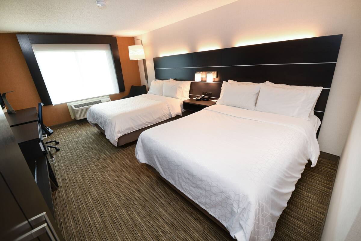 Une chambre d’hôtel avec deux lits, un bureau, une chaise et une grande fenêtre.