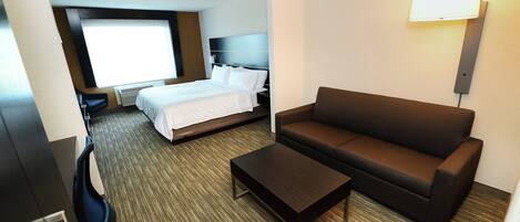 A hotel room with a bed, a sofa, a coffee table, and a desk with a chair.