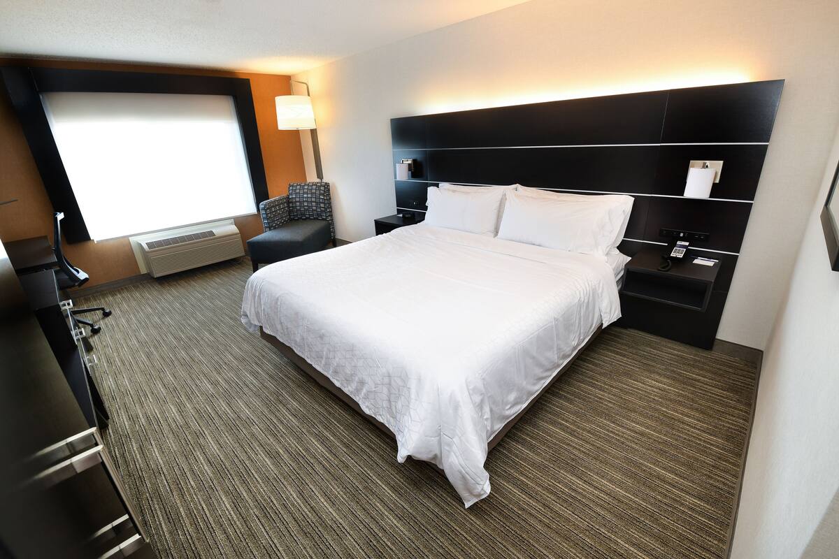 Une chambre d’hôtel avec un grand lit, un bureau, une chaise, une table de chevet, une lampe et une fenêtre avec des stores.
