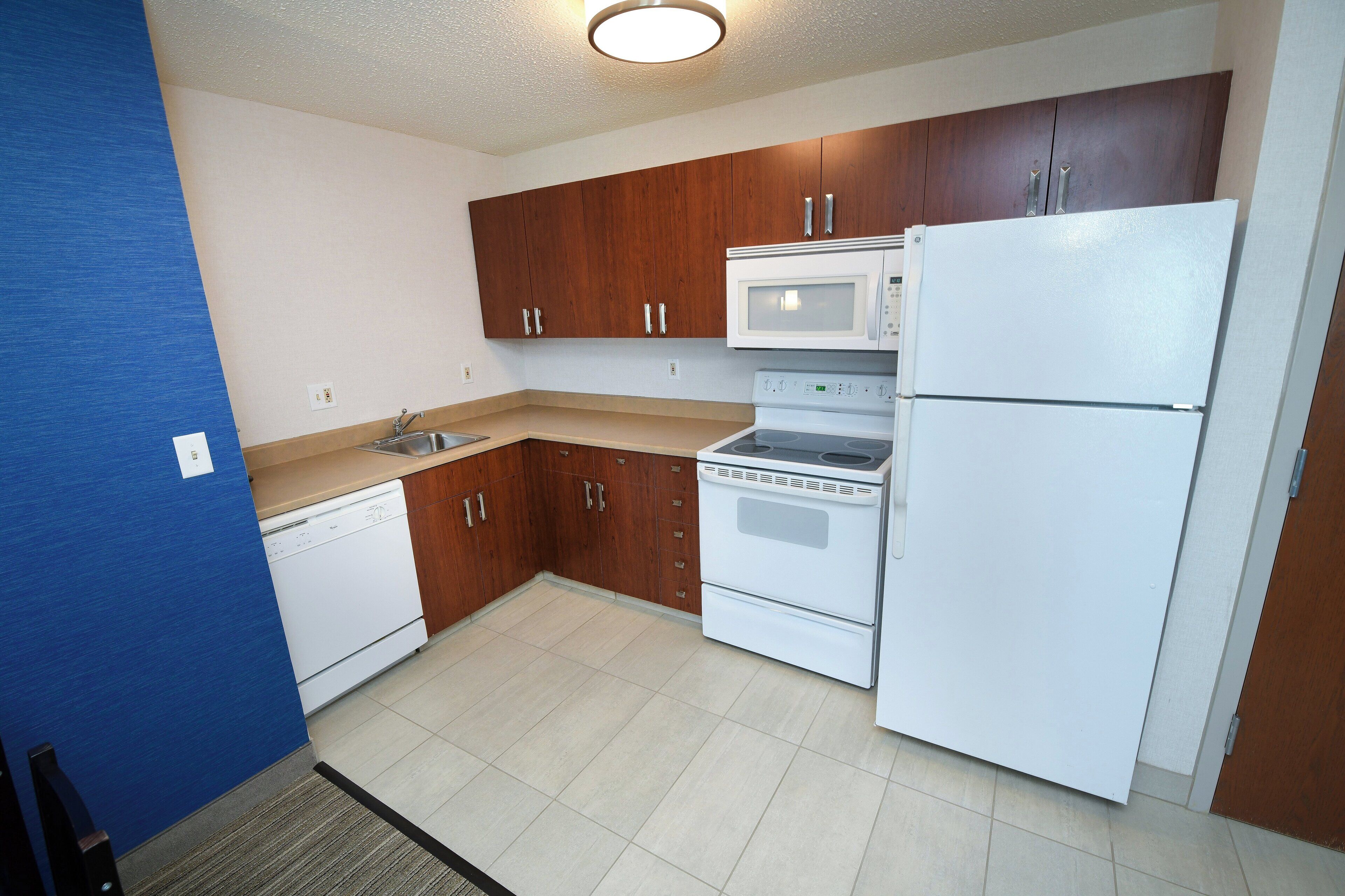 A compact kitchen with wooden cabinets, a white refrigerator, a microwave, and a dishwasher.