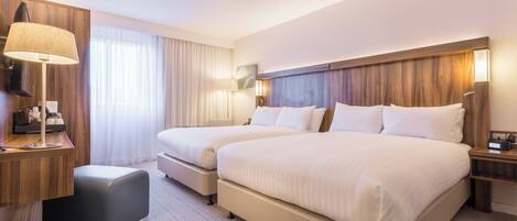 A hotel room with two beds, a desk, a lamp, and a nightstand.