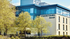 Een Courtyard Marriott hotel met een moderne glazen gevel, omgeven door bomen en een verzorgd gazon.