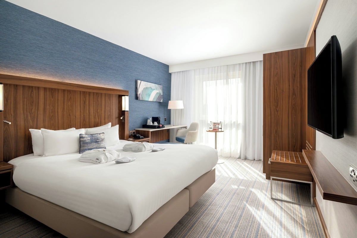 Ein Hotelzimmer mit einem großen Bett, einem Schreibtisch, einem Sessel, einem Fernseher und einem Fenster mit Vorhängen.