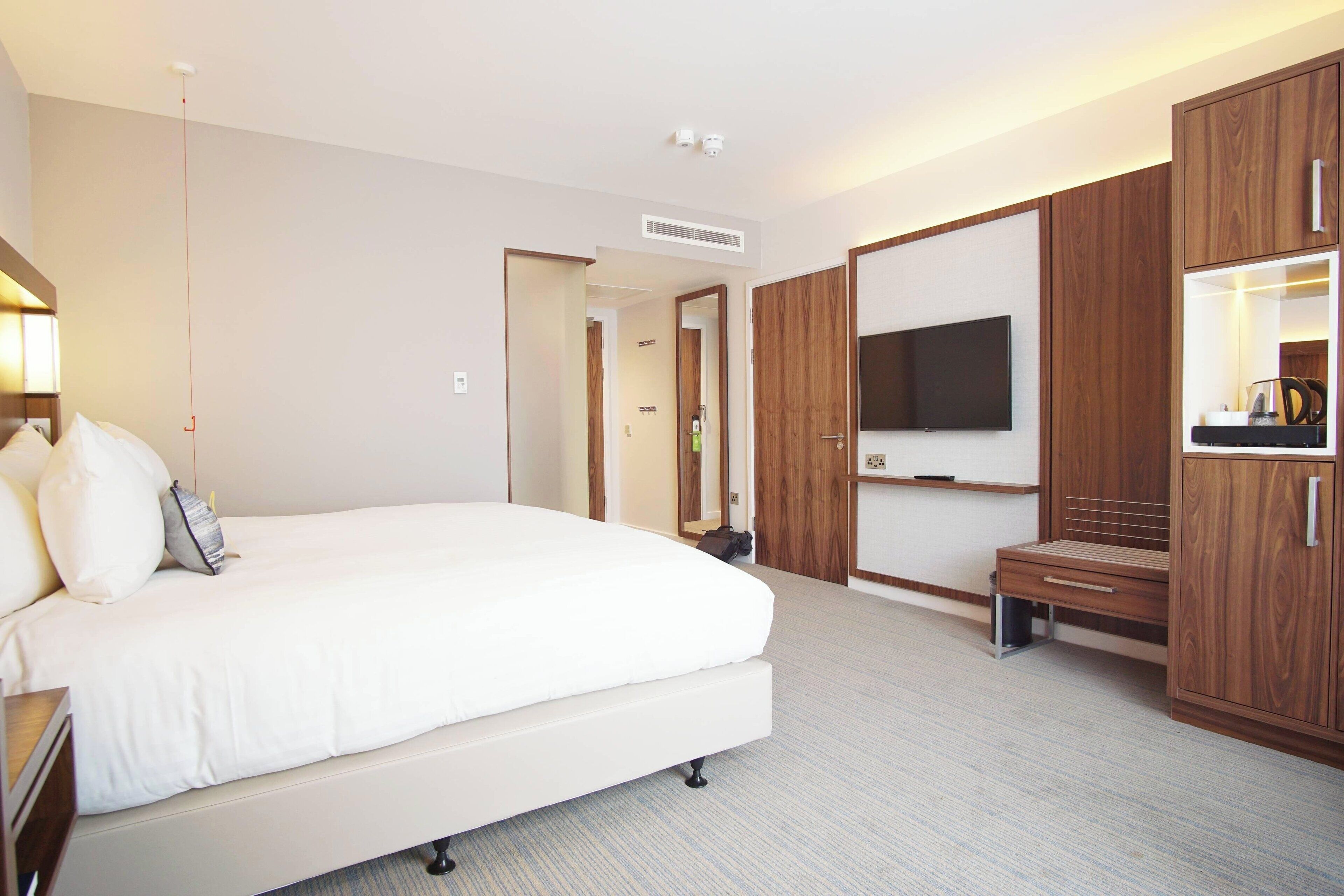 Una habitación de hotel moderna con una cama grande, un armario de madera, un televisor y una pequeña zona de estar.
