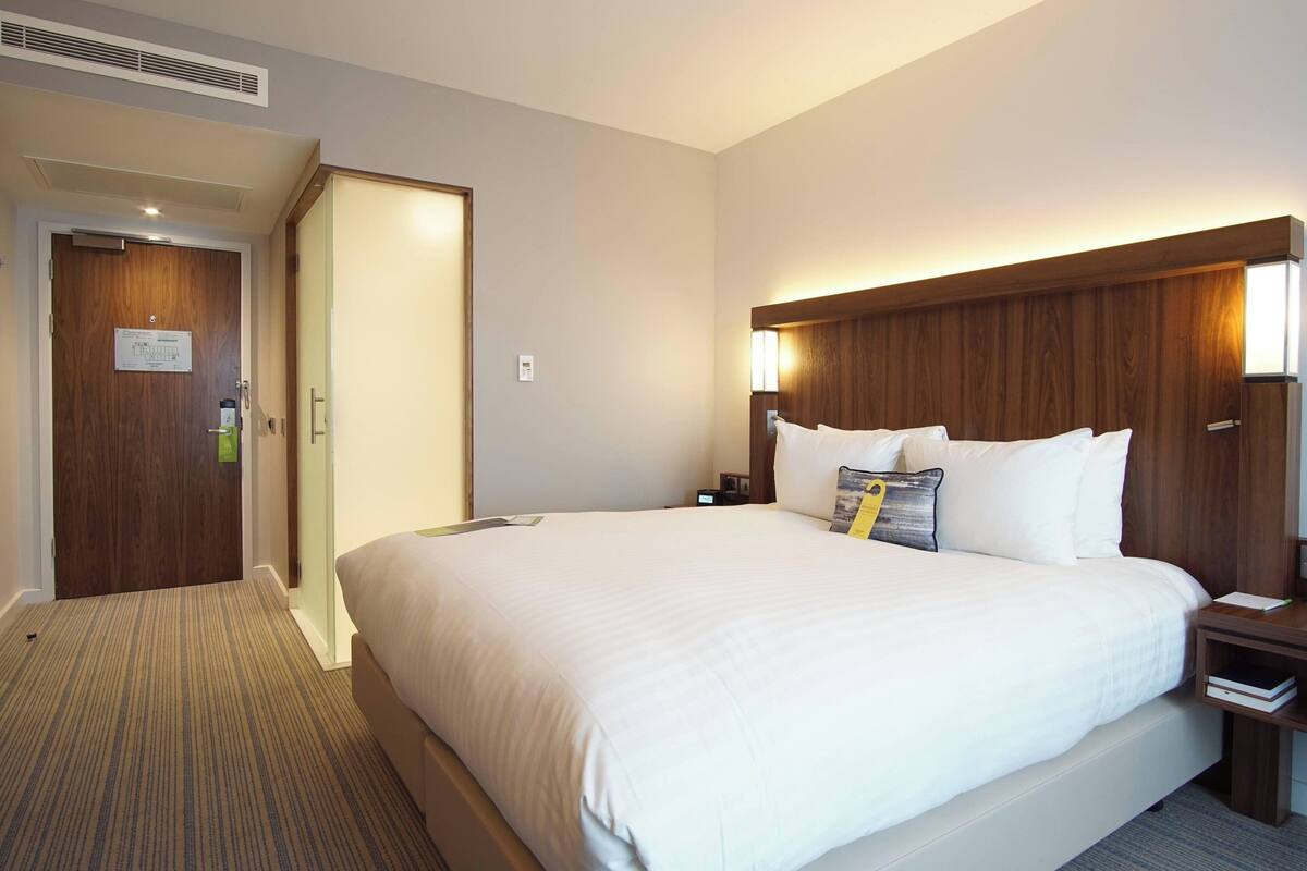 Ein Hotelzimmer mit einem großen Bett, einem Holzkopfstück, Nachttischen und einem Teppichboden.