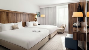 Een hotelkamer met twee bedden, een bureau, een stoel en een groot raam met gordijnen.